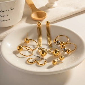 Minimalist gold ball stud and hoop earring set displayed in a white ceramic dish