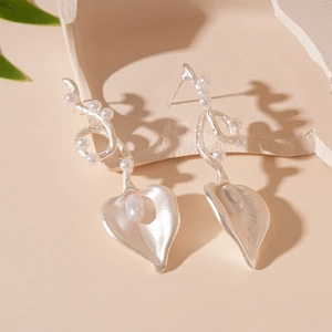 Detail of silver knot earrings with baroque faux pearls and metallic leaf design
