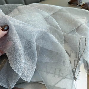 Detail of grey silk scarf with gold thread texture held by hand with subtle shimmer