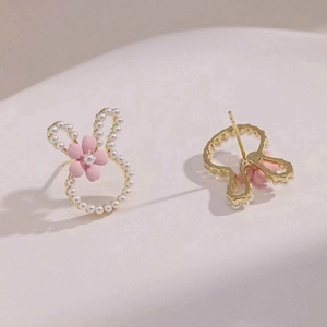 Close-up of golden rabbit stud earrings with white pearl inlay and pink flower detail