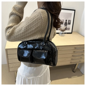 Detail of glossy black shoulder bag with two front pockets and silver zipper on a model