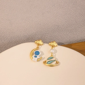 Asymmetric gold earrings with astronaut and planet charms featuring pearl details