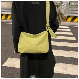 Outdoor shot of an avocado green nylon dumpling crossbody bag with knot shoulder strap