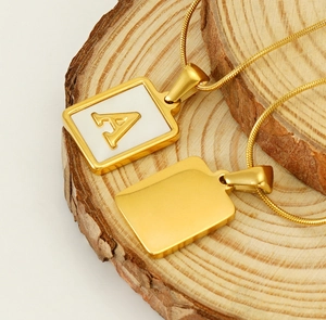 Detail of square gold 18K letter A pendant with natural white shell on wood surface
