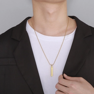 Collier à pendentif barre dorée pour homme porté avec un costume noir et t-shirt blanc