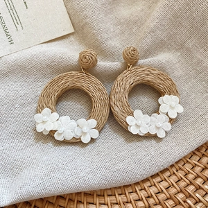 Detail of bohemian rattan circle earrings with white fabric flowers and pearls on linen