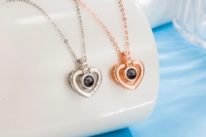 Close-up of heart-shaped projection necklaces in silver and rose gold with LOVE engraving