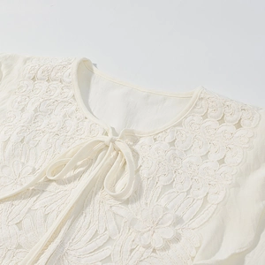 Close-up of white lace embroidered top with delicate floral patterns and neckline tie detail
