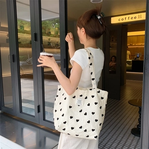 Detail of a textured cream canvas tote bag with black heart prints and a woven label tag