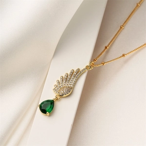 Detailed view of gold wing necklace with clear stones and green teardrop gemstone
