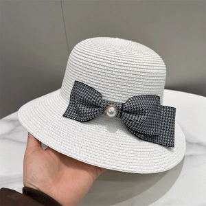 Detail of white woven straw hat featuring a gingham bow and elegant faux pearl embellishment