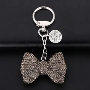 Sparkling rhinestone bow keychain with silver ring on black leather background