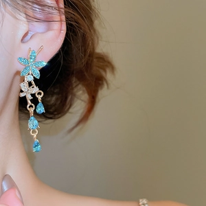 Macro view of long gold drop earrings with blue crystal flowers and teardrop accents