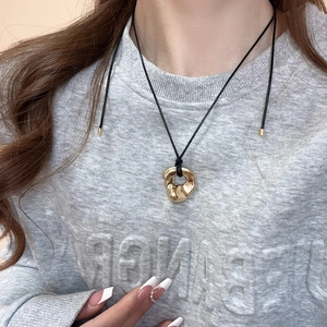 Detail of a minimalist gold irregular ring pendant on a black cord worn by a model