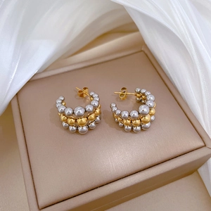 Close-up of dual-tone gold and silver beaded C-shape earrings on elegant silk fabric