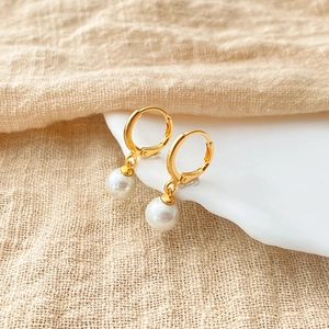 Detailed close-up of small gold earrings with polished white pearls on a ceramic edge
