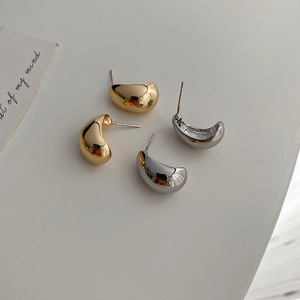 Close-up of geometric C-shaped bean stud earrings in polished gold and silver metal finishes
