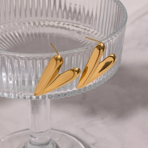 Macro close-up of minimalist gold heart-shaped stud earrings on a textured glass tray