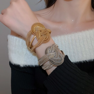 Detail of chunky gold knot cuff bracelet with woven metal texture on a woman's wrist