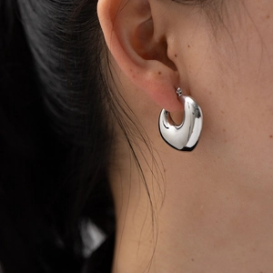 Close-up of a chunky silver-tone hollow hoop earring worn on a model ear