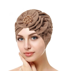 Detail of a brown turban hat with a large pleated flower and pearl bead centerpiece