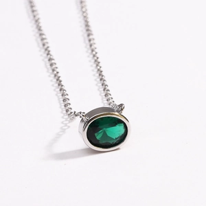 Detailed view of an oval green emerald pendant with a polished silver chain on white background