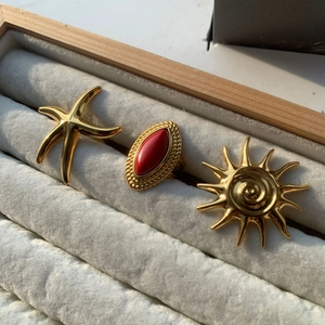 Detailed shot of gold stainless steel rings with starfish, sun motifs and red agate