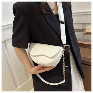 Detailed view of white saddle bag with wide fabric strap and golden decorative chain
