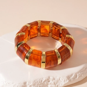 Detail view of amber acrylic stretch bracelet with gold metal spacers on stone surface