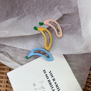 Detailed view of banana-shaped cream hair clips in pink, yellow, and blue colors
