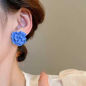 Close-up of a blue resin flower stud earring with layered petals worn on the ear