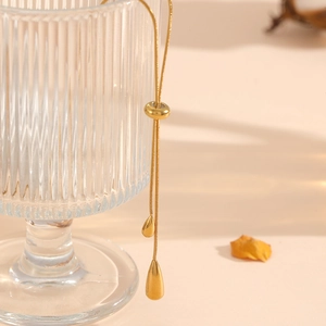 Adjustable gold plated snake chain necklace with teardrop pendants on a glass edge