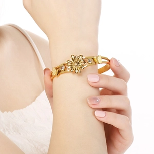 Gros plan d'un bracelet doré avec tournesol et papillon serti de zircons sur le poignet