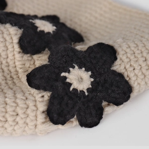 Gros plan sur un chapeau seau en tricot beige avec des fleurs décoratives noires