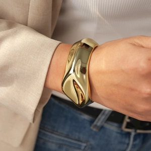 Detail of a chunky gold irregular twisted open cuff bracelet on a model's wrist