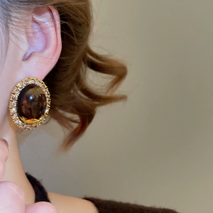 Close-up of elegant amber resin oval stud earrings with crystal halo in gold finish