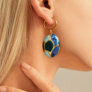 Close-up of gold oval enamel earrings with geometric patterns on model ear