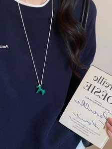 Detail of a bright green horse-shaped pendant on a minimalist cream rope necklace