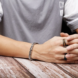 Detail of silver imperial chain bracelet and black steel rings worn by male model