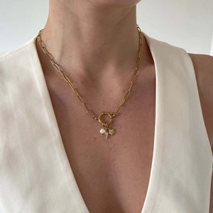 Detail of gold paperclip chain necklace featuring pearl and star charms on model