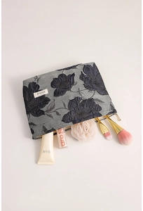 Detailed view of dark blue jacquard makeup bag with gold zipper and floral pattern