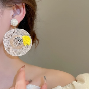 Close-up of oversized raffia straw hat earrings with a yellow flower for beach style