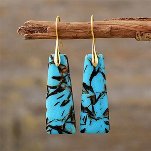 Detailed macro view of bohemian teal stone drop earrings hanging on a rustic wood branch