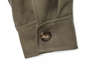Détail du poignet d'une veste en daim vert olive avec double surpiqûre et bouton tortue