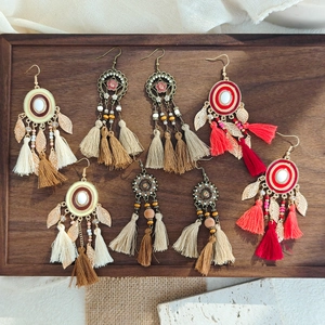 Detailed view of bohemian tassel earrings with beads and feathers in a wooden tray
