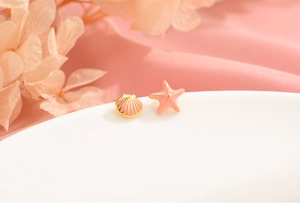 Macro shot of pink enamel starfish and shell stud earrings with gold plating