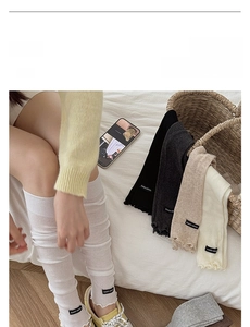 Detail of knitted leg warmers in various colors with suxin aimin label on a white bed