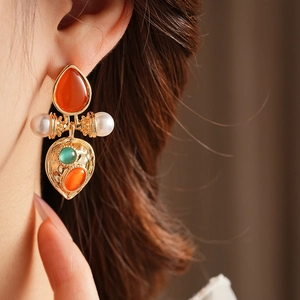 Close-up of vintage gold earrings with orange teardrop stone and pearl details on a model