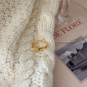 Detailed view of adjustable gold knot ring on soft white knit fabric background
