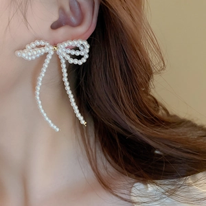Close-up of elegant white pearl bow tassel earrings worn on a model's ear